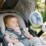 Mother pushing baby in stroller with breathable mesh sunshade in park.